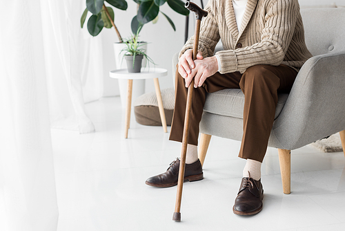 cropped view of senior man sitting in armchair with walking cane