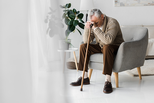 upset retired man sitting in armchair with walking cane at home