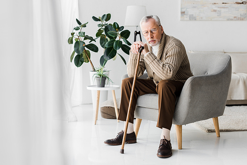 upset retired man sitting in armchair with walking cane and 