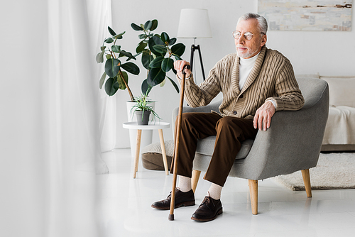 retired man in glasses sitting in armchair with walking cane