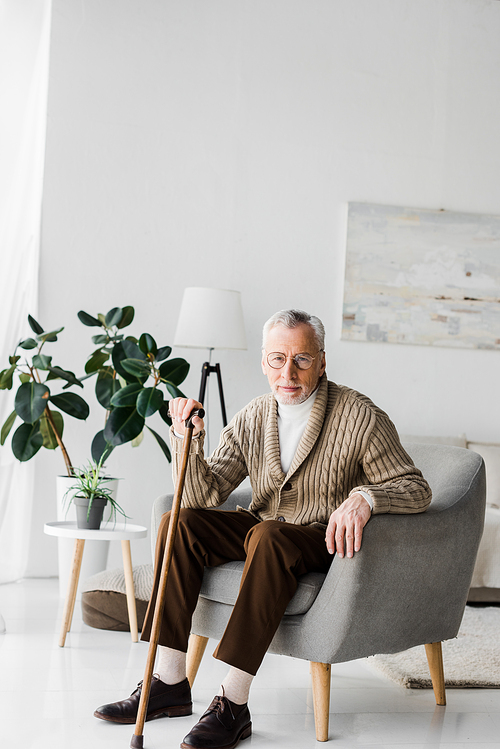 retired man sitting in armchair with walking cane and 