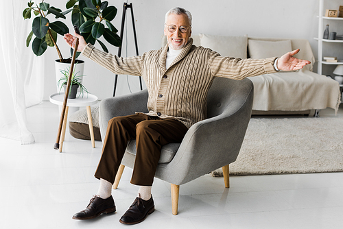 happy retired man in glasses sitting in armchair with outstretched hands