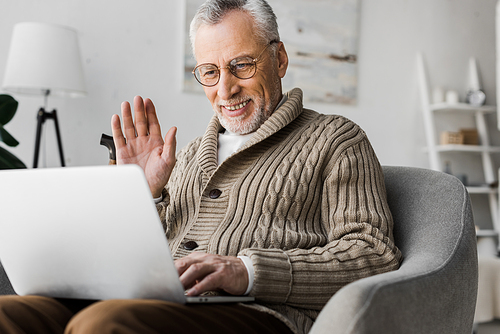 cheerful senior man in glasses waving hand while having video call