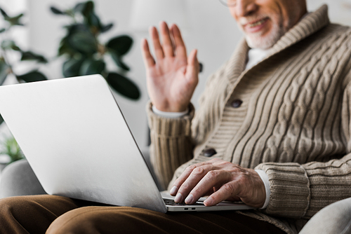 cropped view of cheerful senior man in glasses waving hand while having video call