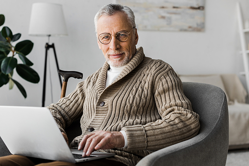 senior man in glasses  while sitting with laptop at home