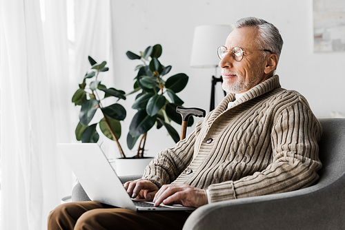 happy senior man in glasses using laptop at home