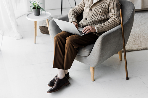 cropped view of senior man in glasses using laptop while sitting with crossed legs