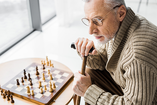 overhead view of retired man in glasses thinking while sitting near chess board at home