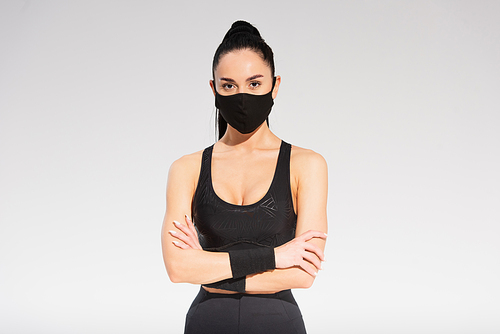 young sportswoman in sportswear and black protective mask standing with crossed arms on grey