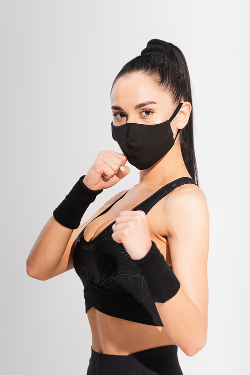 young fighter in sportswear and black protective mask with clenched fists on grey