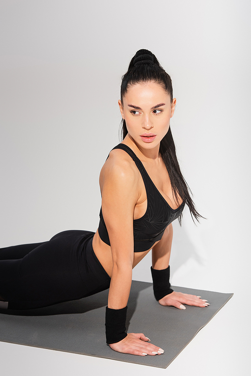 young woman in black sportswear exercising on fitness mat on grey