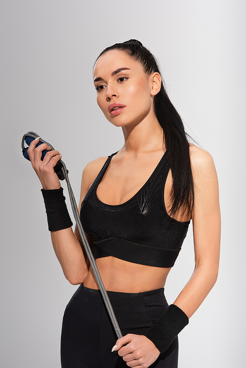 young sportive woman holding skipping rope on grey