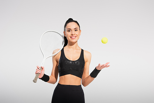 young sportswoman holding tennis racket and throwing ball on grey