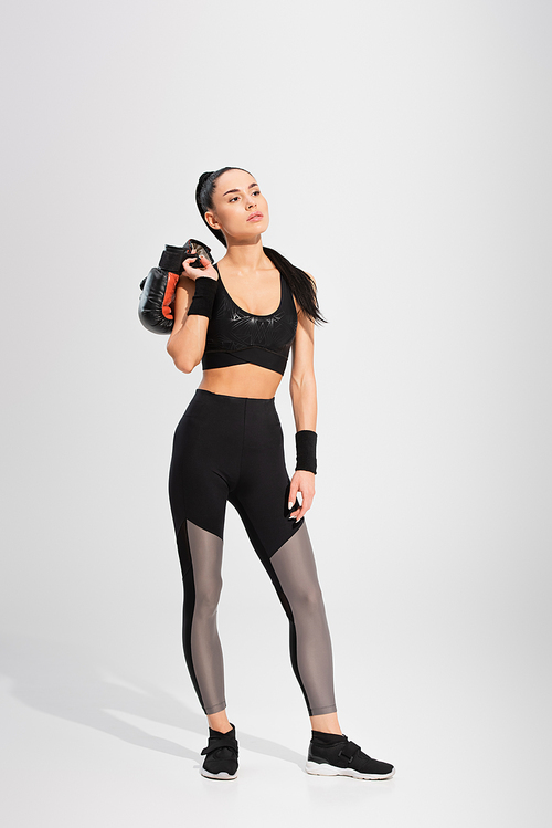 full length of brunette young sportswoman holding boxing gloves on grey