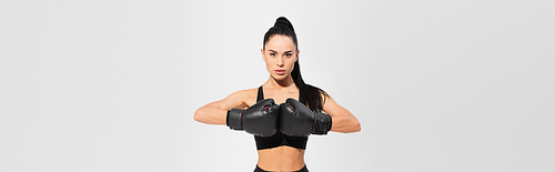 brunette young sportswoman in boxing gloves isolated on grey, banner