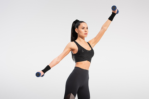 strong woman in black sportswear working out with dumbbells isolated on grey