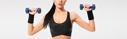 cropped view of strong young sportswoman working out with dumbbells isolated on grey, banner