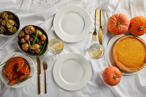top view of served dinner with pumpkin pie, baked vegetables and fresh whole pumpkins on white tablecloth