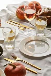 table with white tablecloth served with glasses of rose wine and lemon water, cutlery and whole pumpkins