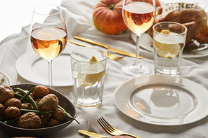 festive thanksgiving dinner with baked vegetables, glasses with rose wine and whole pumpkins on white marble table