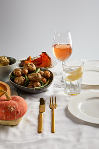 baked potatoes, sliced and whole pumpkin near glasses with rose wine and lemon water isolated on grey