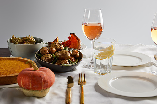 baked vegetables, pumpkin pie and whole pumpkin near glasses with rose wine and lemon water isolated on grey