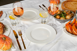 festive dinner with baked seasonal vegetables near glasses with rose wine and lemon water served on white tablecloth