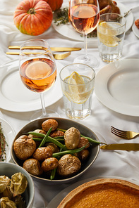 festive dinner with baked seasonal vegetables near glasses with rose wine and lemon water served on white tablecloth