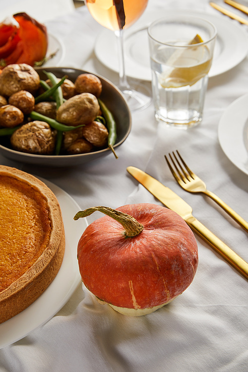 baked potatoes and pumpkin pie near whole pumpkin on white tablecloth