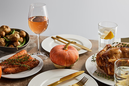 Thanksgiving day dinner with baked vegetables, grilled turkey and glasses with rose wine and lemon water isolated on grey