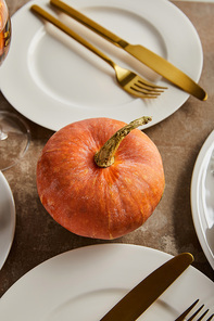 whole ripe pumpkin near white plates with golden knives and forks on stone table