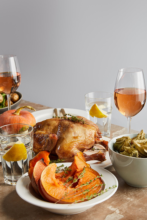 sliced baked pumpkin near grilled turkey and glasses with rose wine on stone table isolated on grey