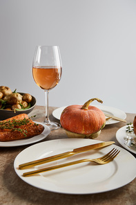 plate with golden knife and fork near whole pumpkin and glass with rose wine isolated on grey