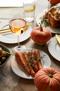 grilled carrot with rosemary near whole pumpkins and glasses with rose wine and lemonade on stone table