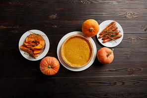 top view of whole pumpkins, pumpkin pie, baked whole carrot and sliced pumpkin on dark wooden surface