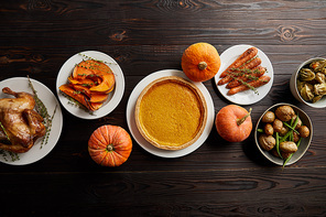 top view of whole pumpkins, pumpkin pie, baked whole carrot and sliced pumpkin, grilled turkey and potato on dark wooden surface