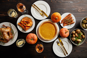 top view of whole pumpkins, pumpkin pie, baked vegetables, grilled turkey and glasses with rose wine and lemon water on dark wooden surface