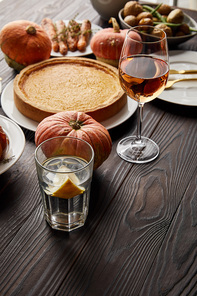 pumpkin pie, glasses with rose wine, baked vegetables and whole pumpkins on dark wooden table