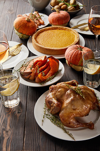 festive dinner with grilled turkey, baked vegetables, pumpkin pie and glasses with rose wine and lemon water on dark wooden table