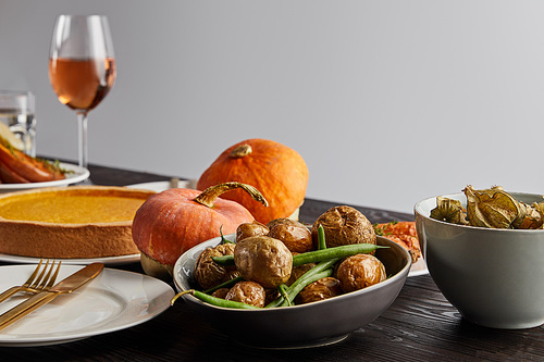 baked pumpkins and potatoes, pumpkin pie and glass with rose wine on wooden table isolated on grey