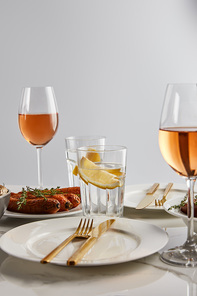 baked carrots, glasses with rose wine and lemon water, white plates and golden cutlery on marble table isolated on grey