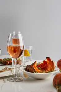 glasses with rose wine, baked pumpkin and carrots served on white marble table isolated on grey