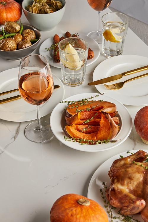 traditional thanksgiving dinner with baked vegetables, glasses with rose wine and lemon water on white marble table