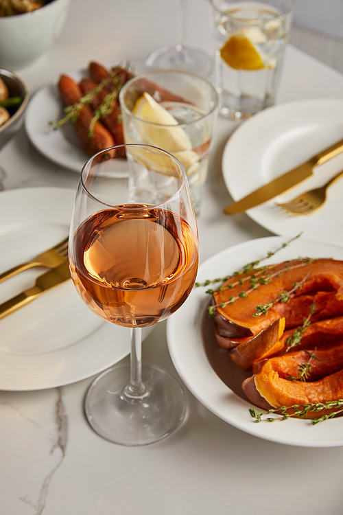selective focus of glass with rose wine near baked sliced pumpkin of marble table