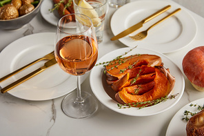 glass with rose wine near baked cut pumpkin and plates with forks and knives on marble table