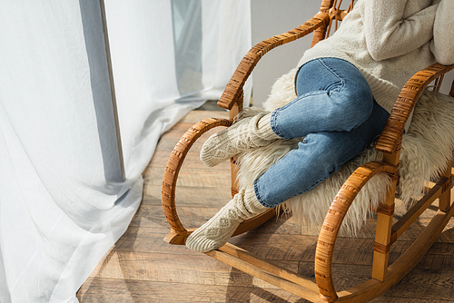 cropped view of woman in jeans and warm socks sitting in rocking chair