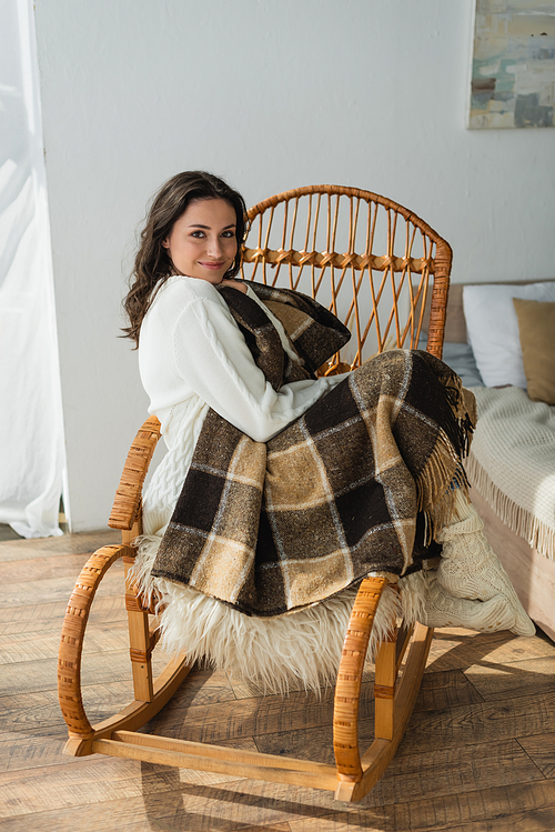 pleased woman  while sitting in wicker chair under plaid blanket