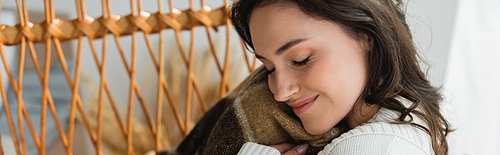 pleased woman with closed eyes holding soft blanket near face, banner