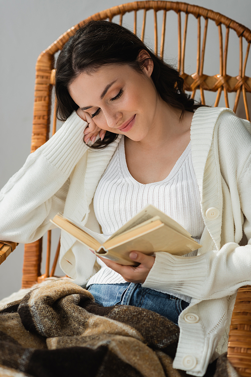 happy young woman sitting in wicker chair and reading novel