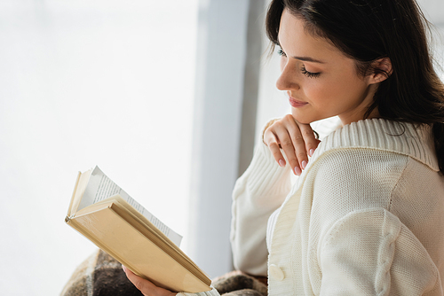 young woman in knitted cardigan reading novel at home